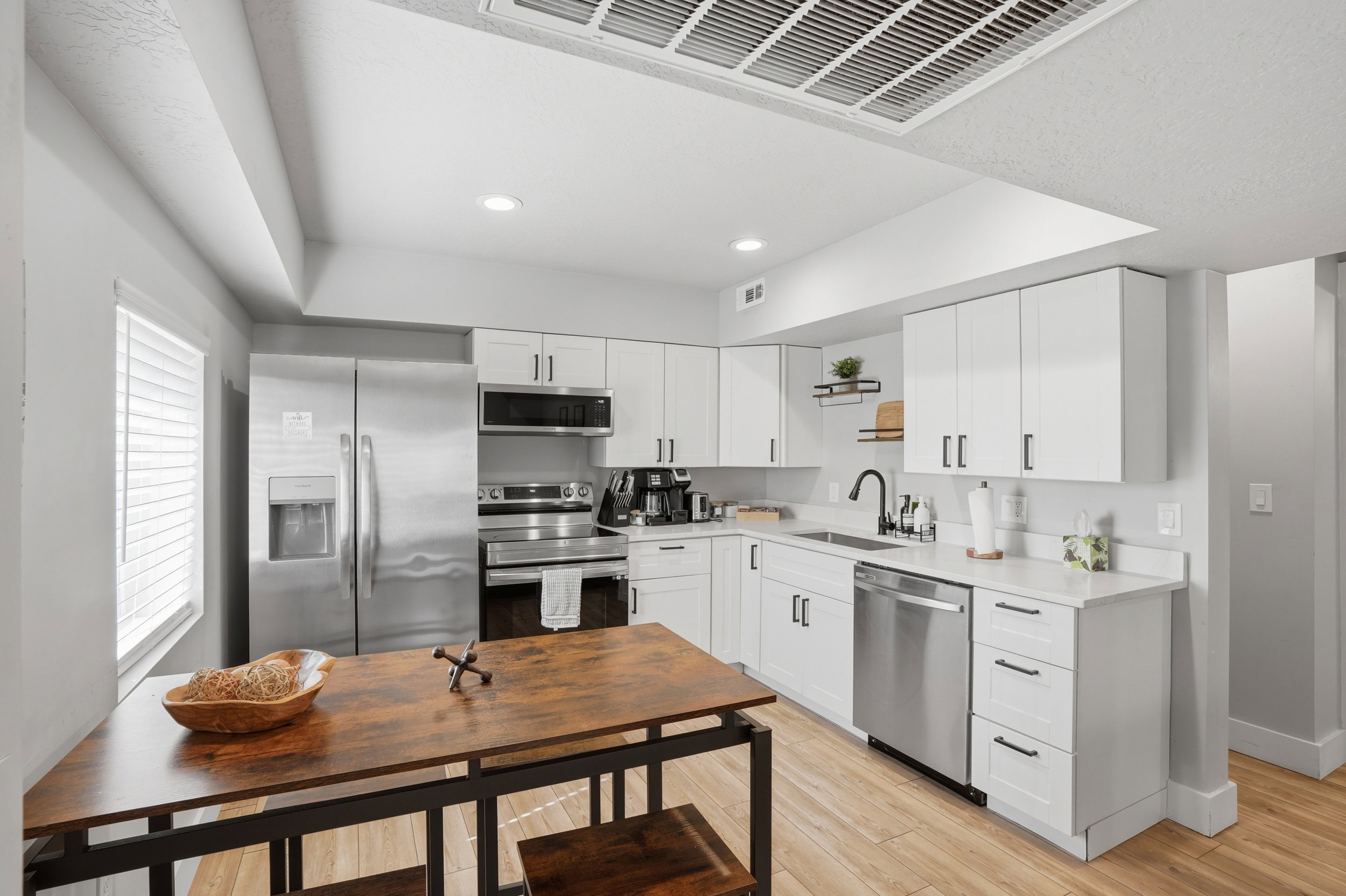 Furnished Unit #44 faces West. Kitchen with stainless steel appliances, white cabinetry, light wood-style floors, recessed lighting, and light stone counters