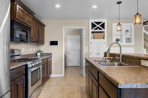 Kitchen with stainless steel appliances, dark wood finish cabinetry, a center island with sink, hanging light fixtures, and a textured ceiling