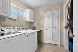 Laundry room featuring washing machine and dryer, a textured ceiling, light tile patterned floors, and cabinet space