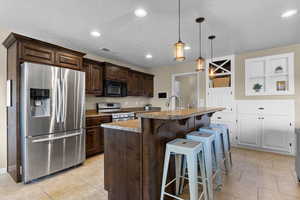 Kitchen featuring stainless steel appliances, a kitchen breakfast bar, an island with sink, dark wood finish cabinetry, and decorative light fixtures