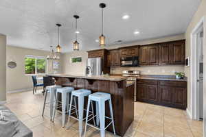 Kitchen featuring stainless steel appliances, dark wood finish cabinetry, a kitchen bar, light tile patterned flooring, and a textured ceiling