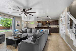 Living room with light tile patterned floors, healthy amount of natural light, ceiling fan, a textured ceiling, and hanging lights