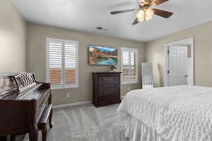 Bedroom featuring light colored carpet, multiple windows, a textured ceiling, and a ceiling fan