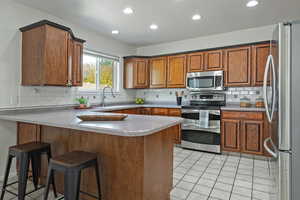 Kitchen featuring a peninsula, light tile patterned flooring, stainless steel appliances, a kitchen breakfast bar, and wood finish cabinetry