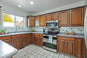 Kitchen featuring stainless steel appliances, light tile patterned floors, wood finish cabinetry, backsplash, and recessed lighting
