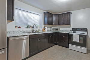 Basement kitchen with stainless steel appliances, dark wood finish cabinetry, and light countertops