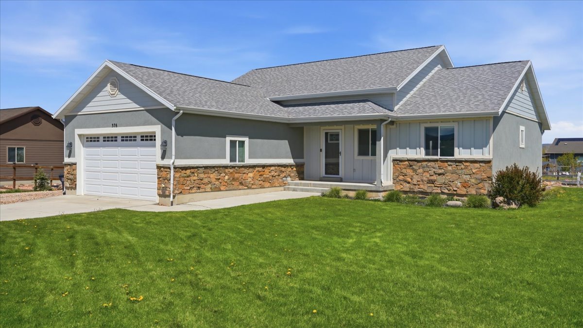 View of front of house with stone siding, board and batten siding, a shingled roof, a garage, and a front yard
