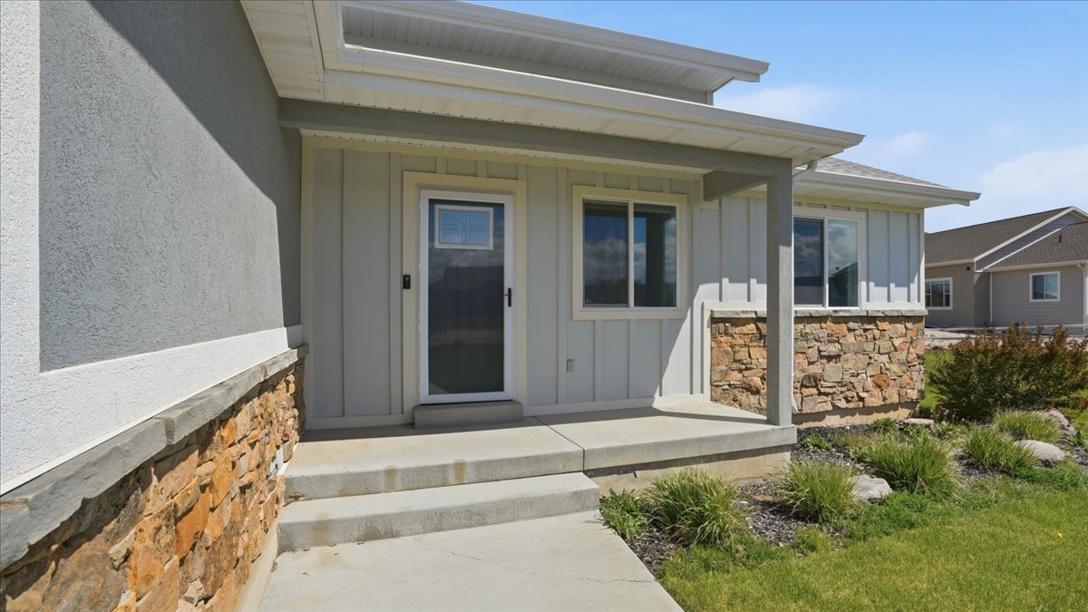 View of exterior entry with board and batten siding, covered porch, and stone siding