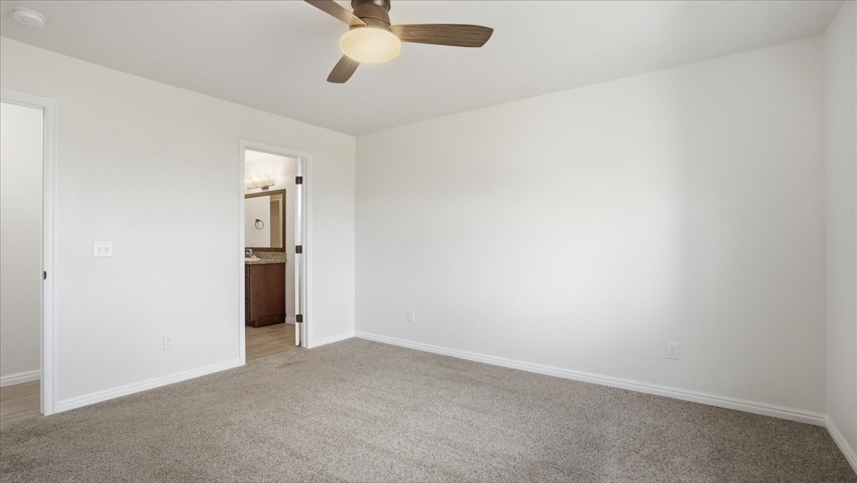 Unfurnished bedroom with light colored carpet, ceiling fan, and connected bathroom