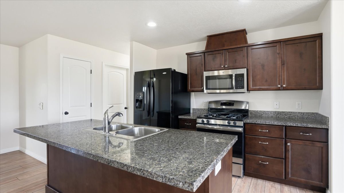 Kitchen featuring dark wood finish cabinetry, stainless steel appliances, an island with sink, light wood-type flooring, and recessed lighting