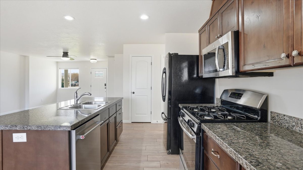 Kitchen with stainless steel appliances, an island with sink, light wood-type flooring, dark stone countertops, and recessed lighting