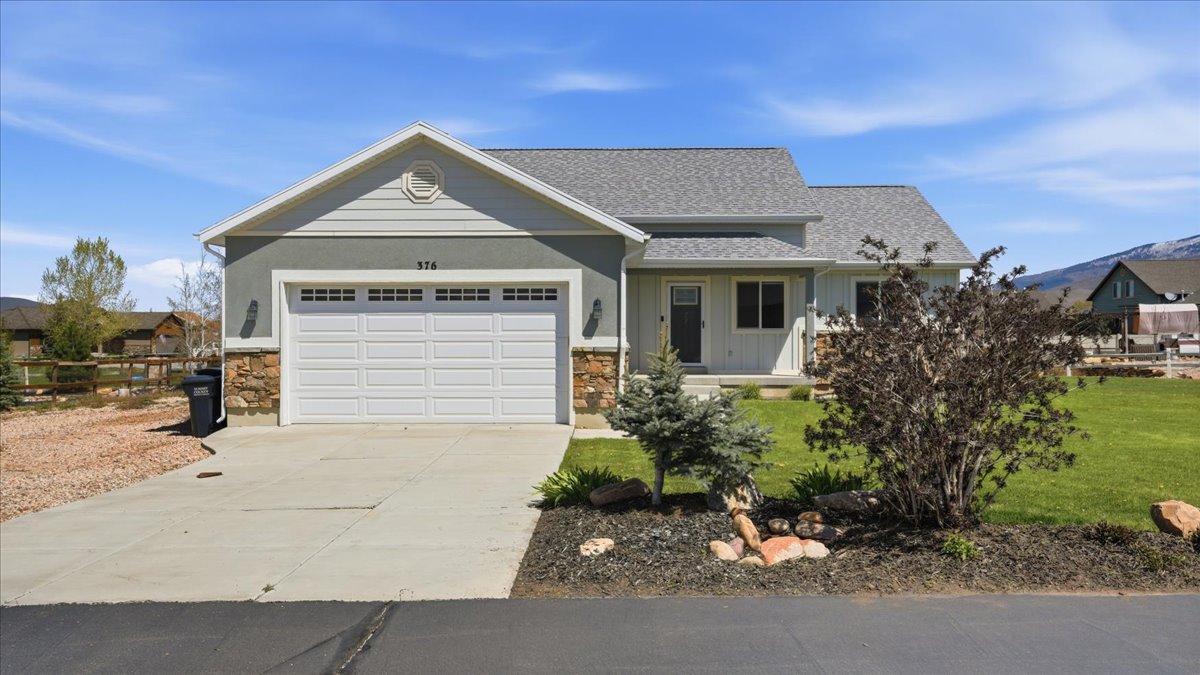 View of front of house with an attached garage, concrete driveway, stone siding, and a front lawn