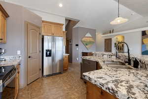 Kitchen with stainless steel appliances, vaulted ceiling, light stone counters, arched walkways, and pendant lighting
