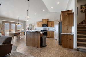 Kitchen with a kitchen island with sink, stainless steel appliances, stone tile flooring, a kitchen breakfast bar, and decorative light fixtures