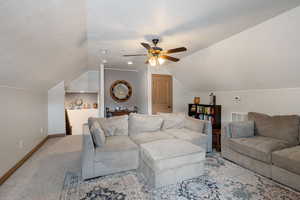 Carpeted living area featuring a ceiling fan and baseboards