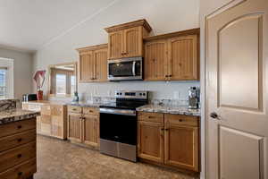 Kitchen with stainless steel appliances, vaulted ceiling, light stone countertops, and wood finish cabinets