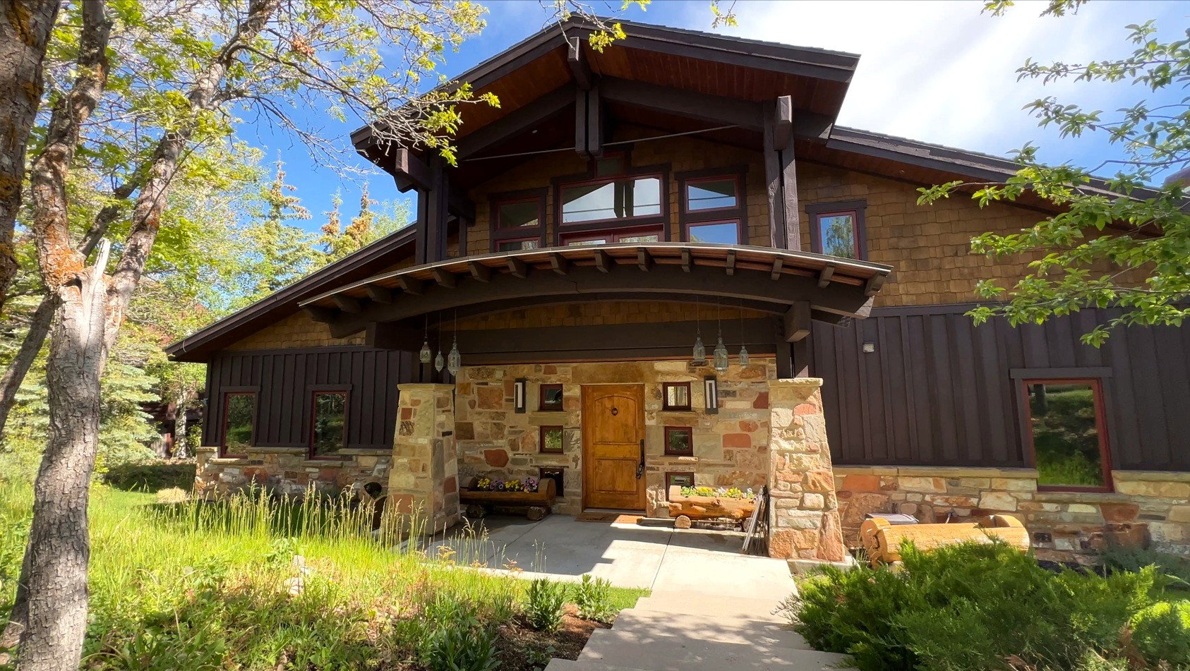 Craftsman-style exterior featuring stone veneer siding, rich brown paneling, cedar shake accents, a prominent covered entry, and a natural wood entry door