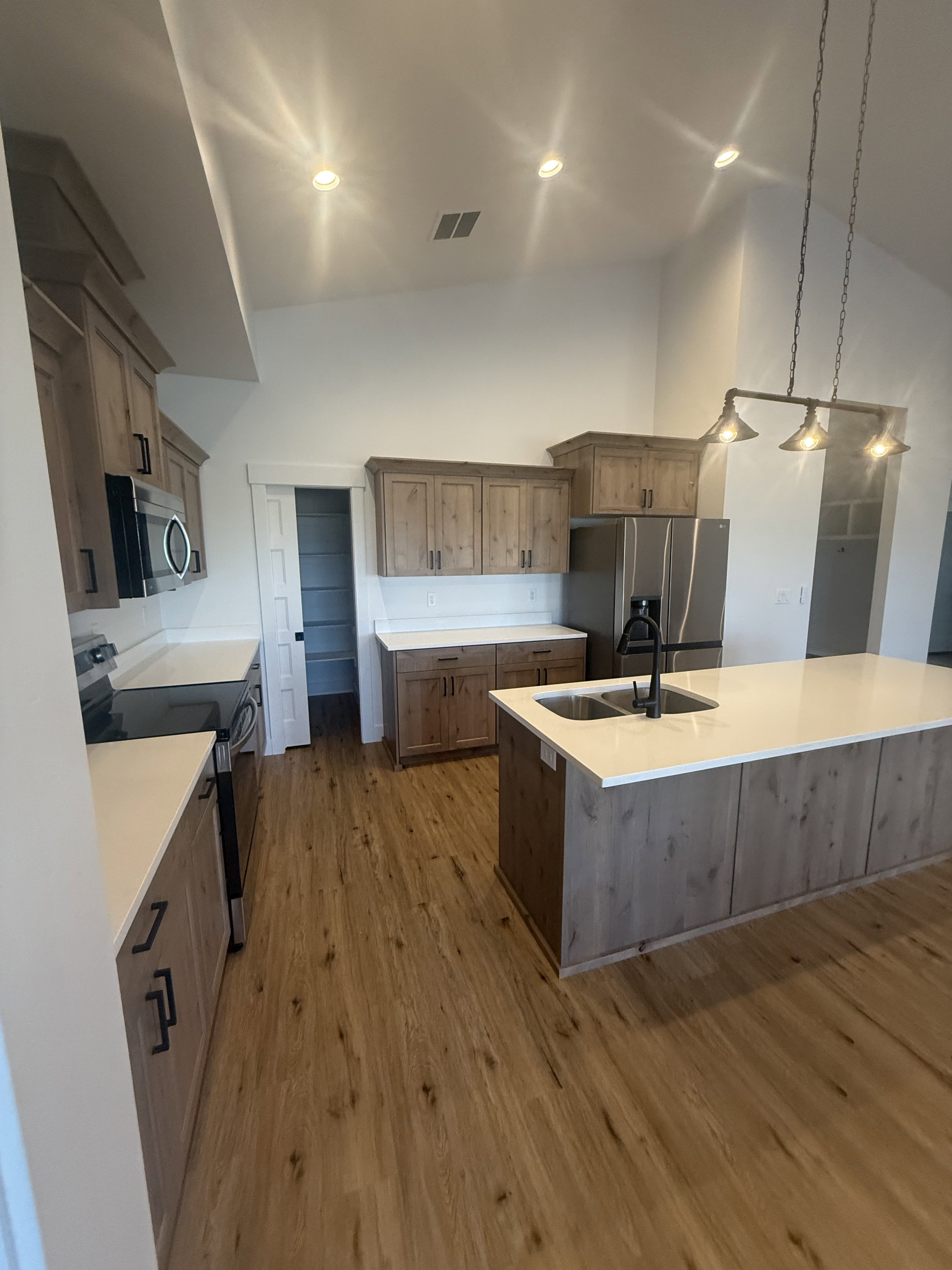 Kitchen featuring stainless steel appliances, a spacious island, light wood-type flooring, vaulted ceiling, and hanging light fixtures
