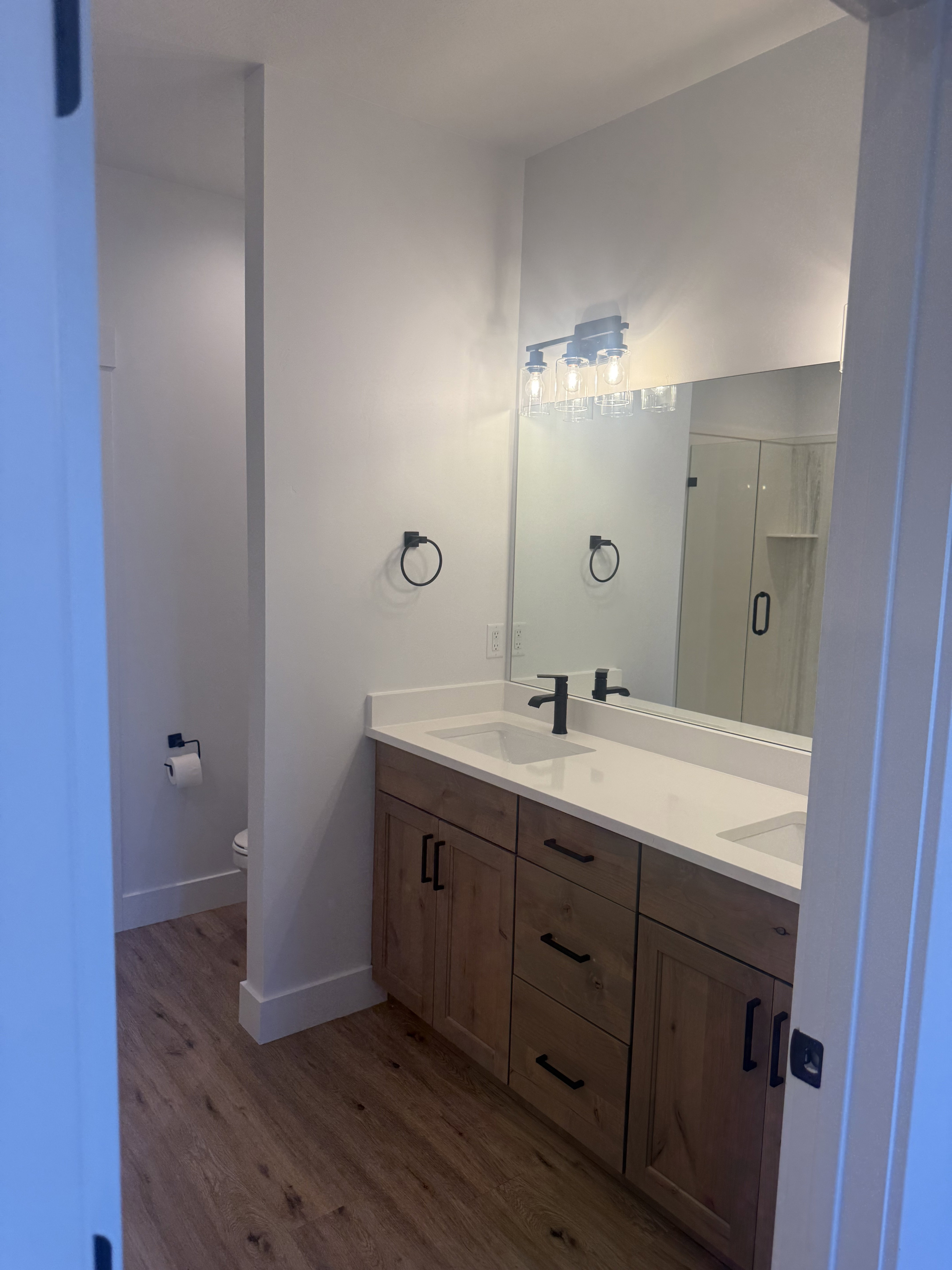 Bathroom featuring double vanity, dark wood-style flooring, and a stall shower
