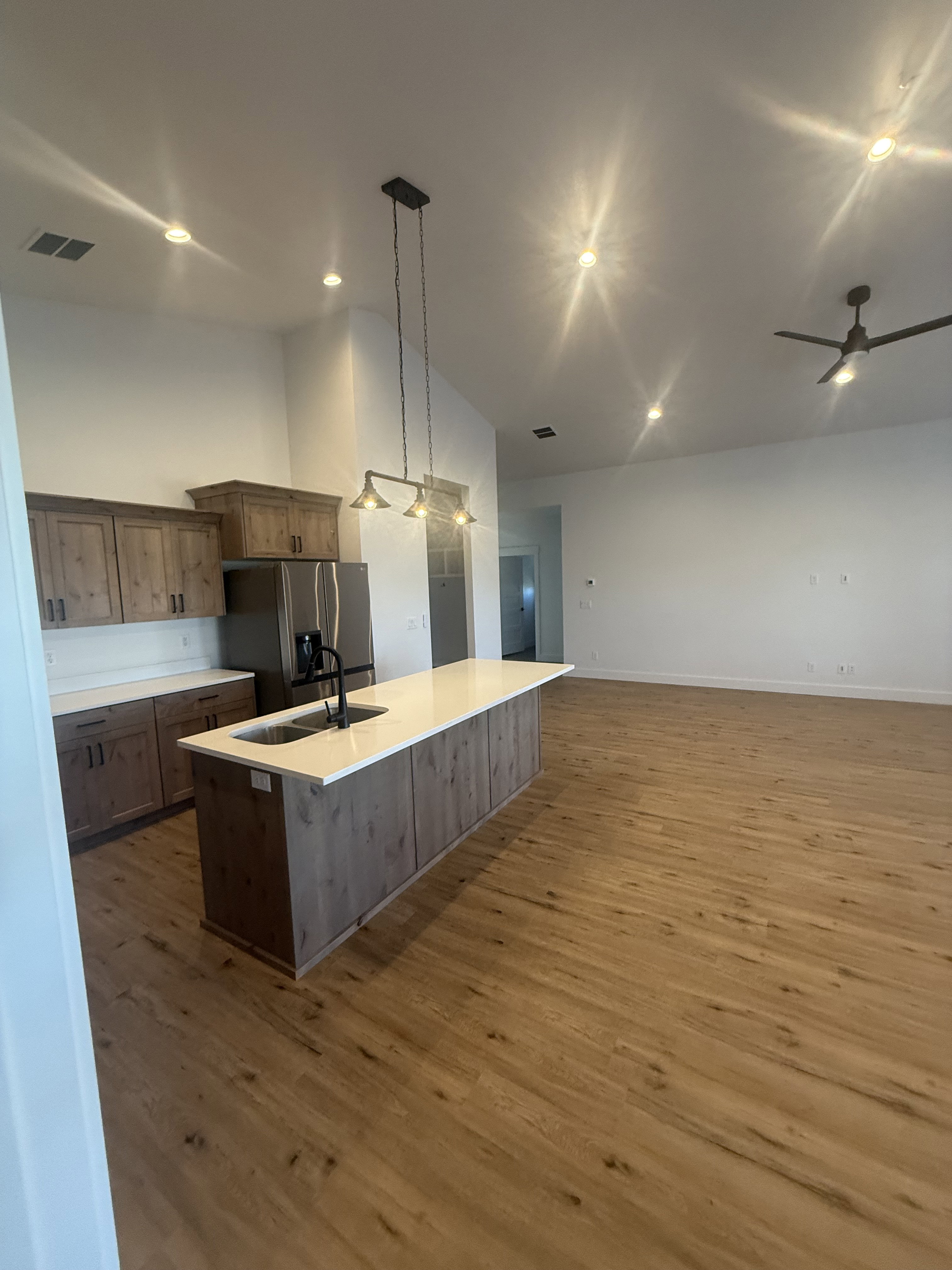 Kitchen featuring an island with sink, stainless steel refrigerator with ice dispenser, light wood-style flooring, hanging light fixtures, and a high ceiling