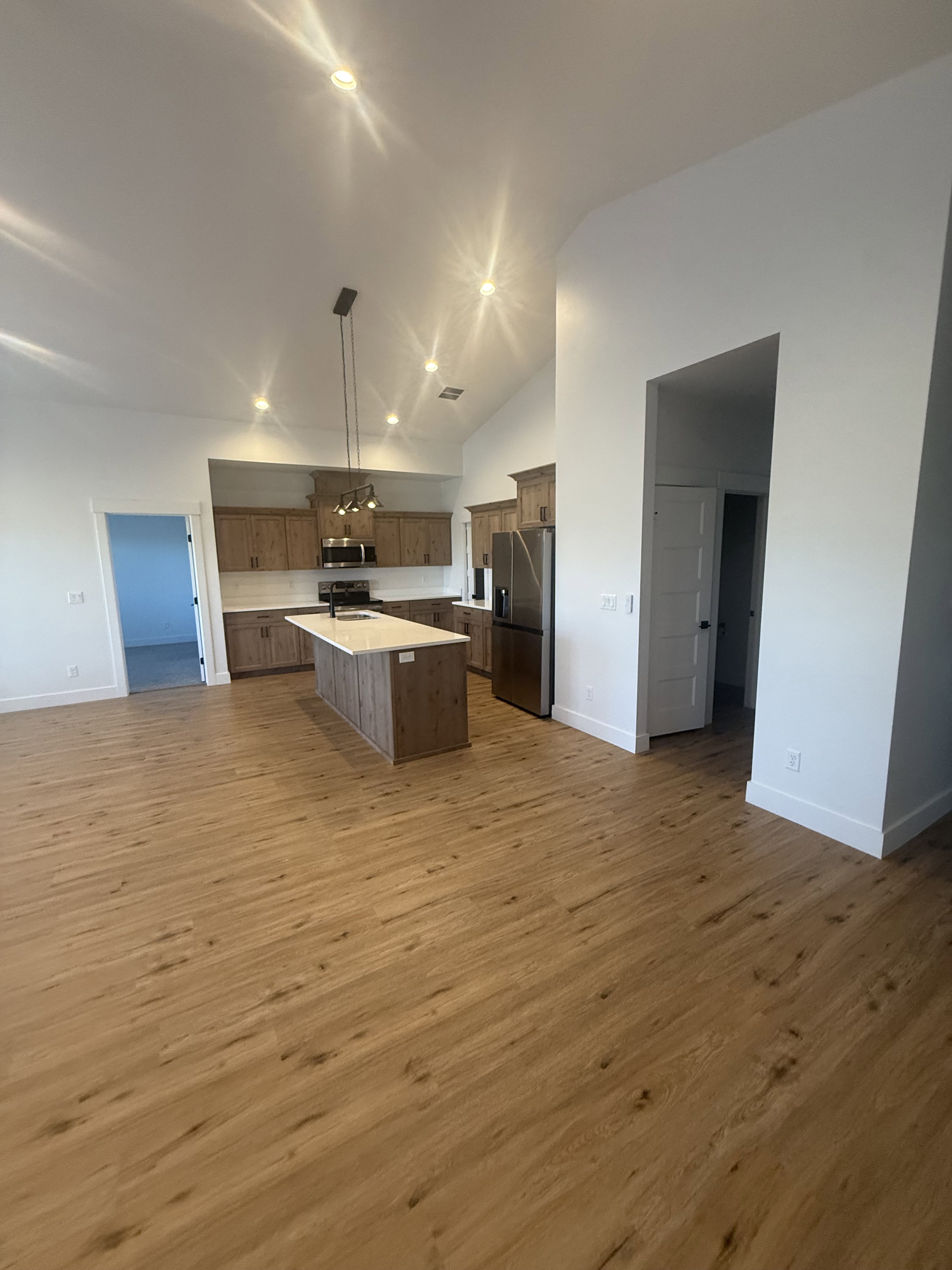 Kitchen with open floor plan, a kitchen island, stainless steel appliances, light wood finished floors, and vaulted ceiling