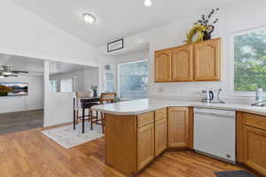 Kitchen with light countertops, a peninsula, vaulted ceiling, white dishwasher, and healthy amount of natural light