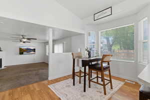 Dining space with light wood-style flooring, a tiled fireplace, lofted ceiling, and a ceiling fan