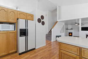 Kitchen with a warm lit fireplace, white appliances, light countertops, light wood-style flooring, and open floor plan