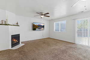 Unfurnished living room featuring a ceiling fan, carpet flooring, a tile fireplace, and a textured ceiling
