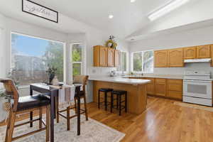 Kitchen featuring vaulted ceiling, light countertops, electric range, a peninsula, and a kitchen bar