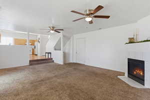 Unfurnished living room featuring a tiled fireplace, light carpet, and a ceiling fan