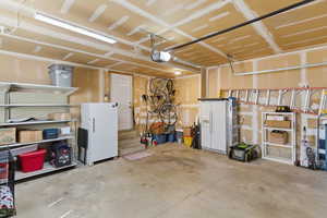 Garage with white refrigerator with ice dispenser, freestanding refrigerator, and a garage door opener