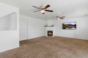 Unfurnished living room featuring a ceiling fan, a fireplace, and carpet floors