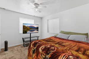 Bedroom with light colored carpet, ceiling fan, and a textured ceiling
