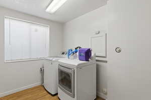 Laundry area featuring washing machine and clothes dryer, light wood-style floors, and a textured ceiling