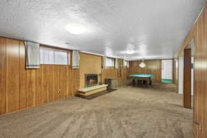 Game room featuring a brick fireplace, carpet, billiards table, a textured ceiling, and wooden walls