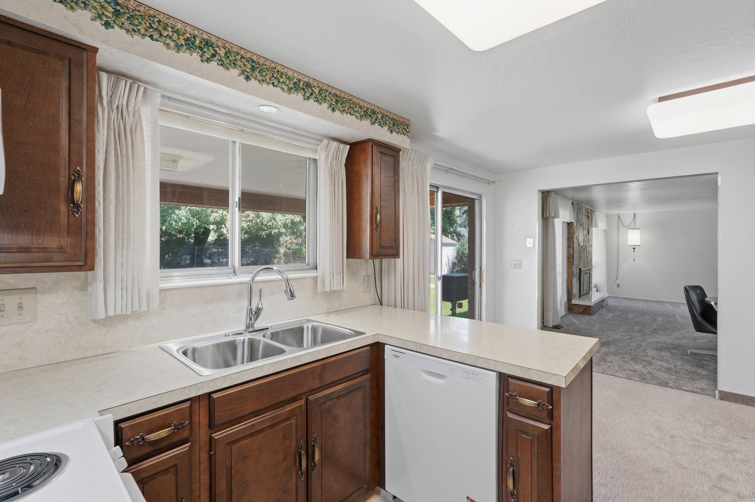 Kitchen featuring wood-finish cabinetry, a double basin stainless steel sink, and light-toned countertops