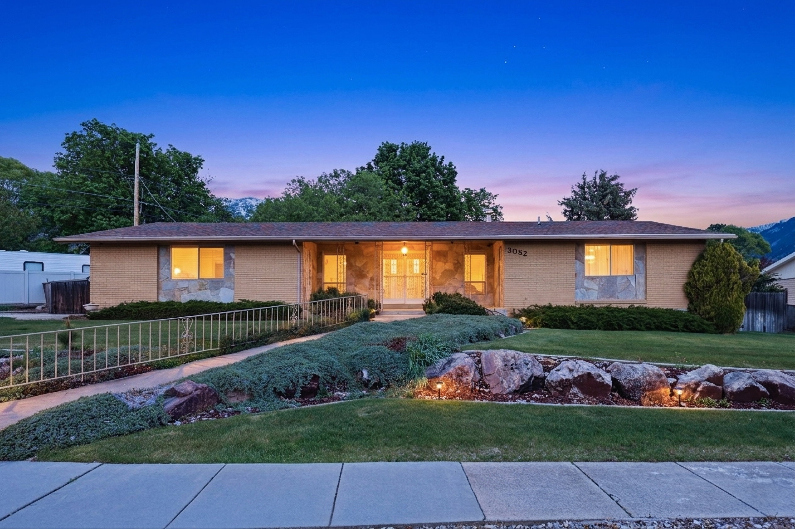 Ranch-style residence featuring a brick facade with stone accents, a landscaped front yard with a ramped walkway, and mature plantings