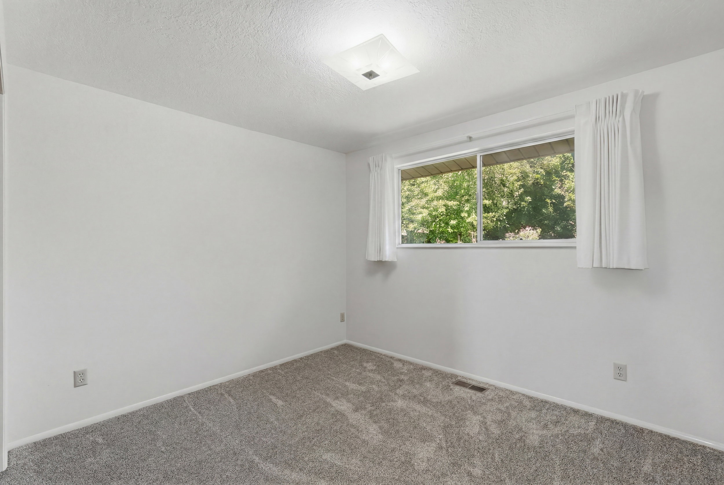 Room featuring soft gray carpeting, white painted walls, and a large window with white curtains