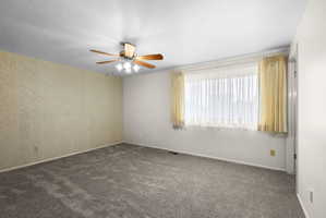 Empty room with ceiling fan, dark colored carpet, and a textured ceiling