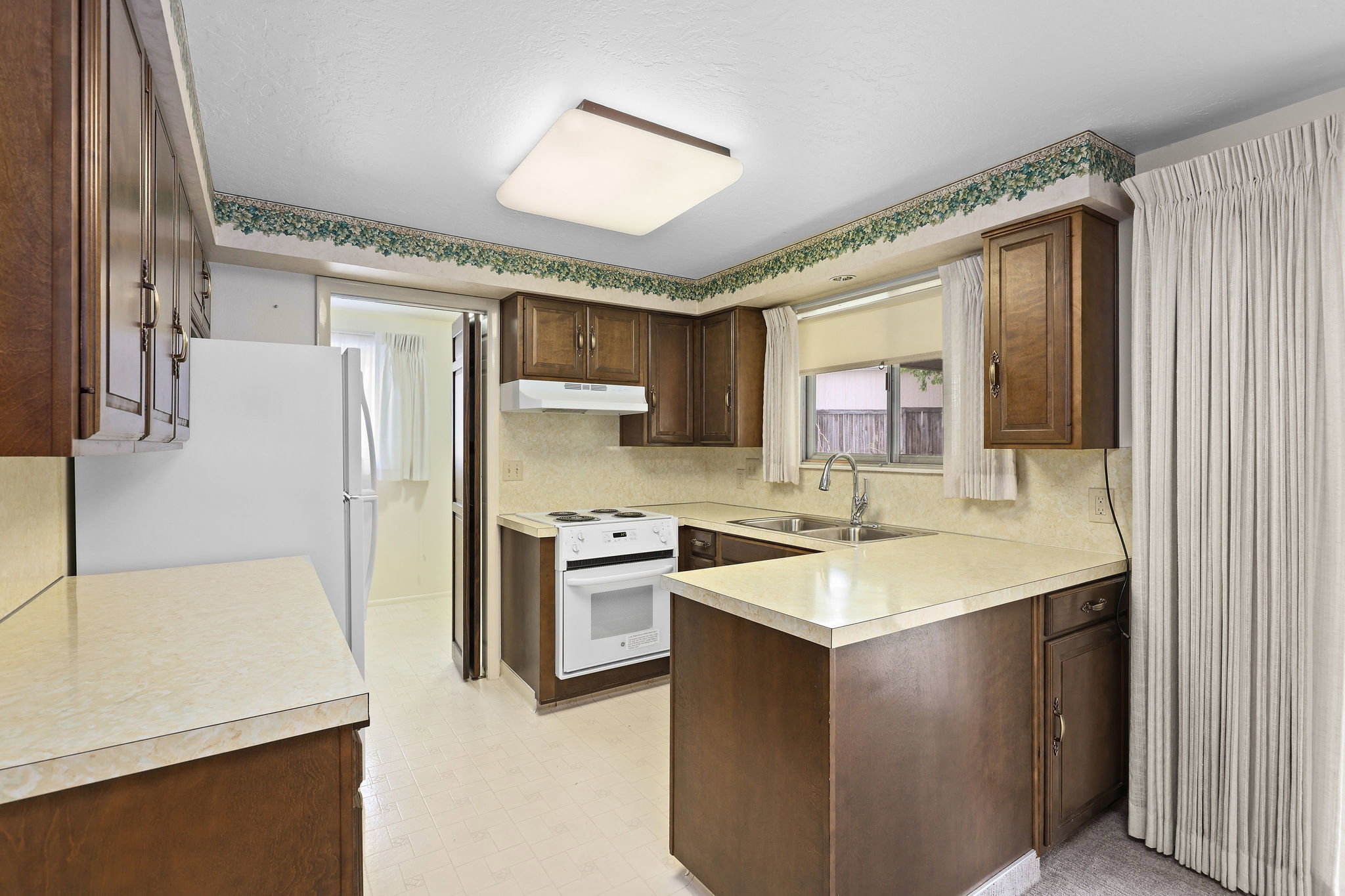 Kitchen featuring light flooring, white appliances, light countertops, dark wood finish cabinets, and a peninsula with new range.