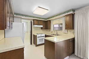 Kitchen featuring light flooring, white appliances, light countertops, dark wood finish cabinets, and a peninsula