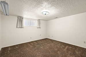 Unfurnished room featuring a textured ceiling and dark colored carpet
