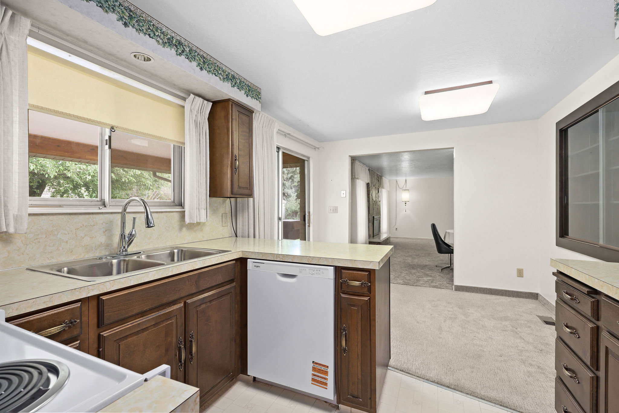 Kitchen with a peninsula, light colored carpet, light countertops, and new dishwasher.