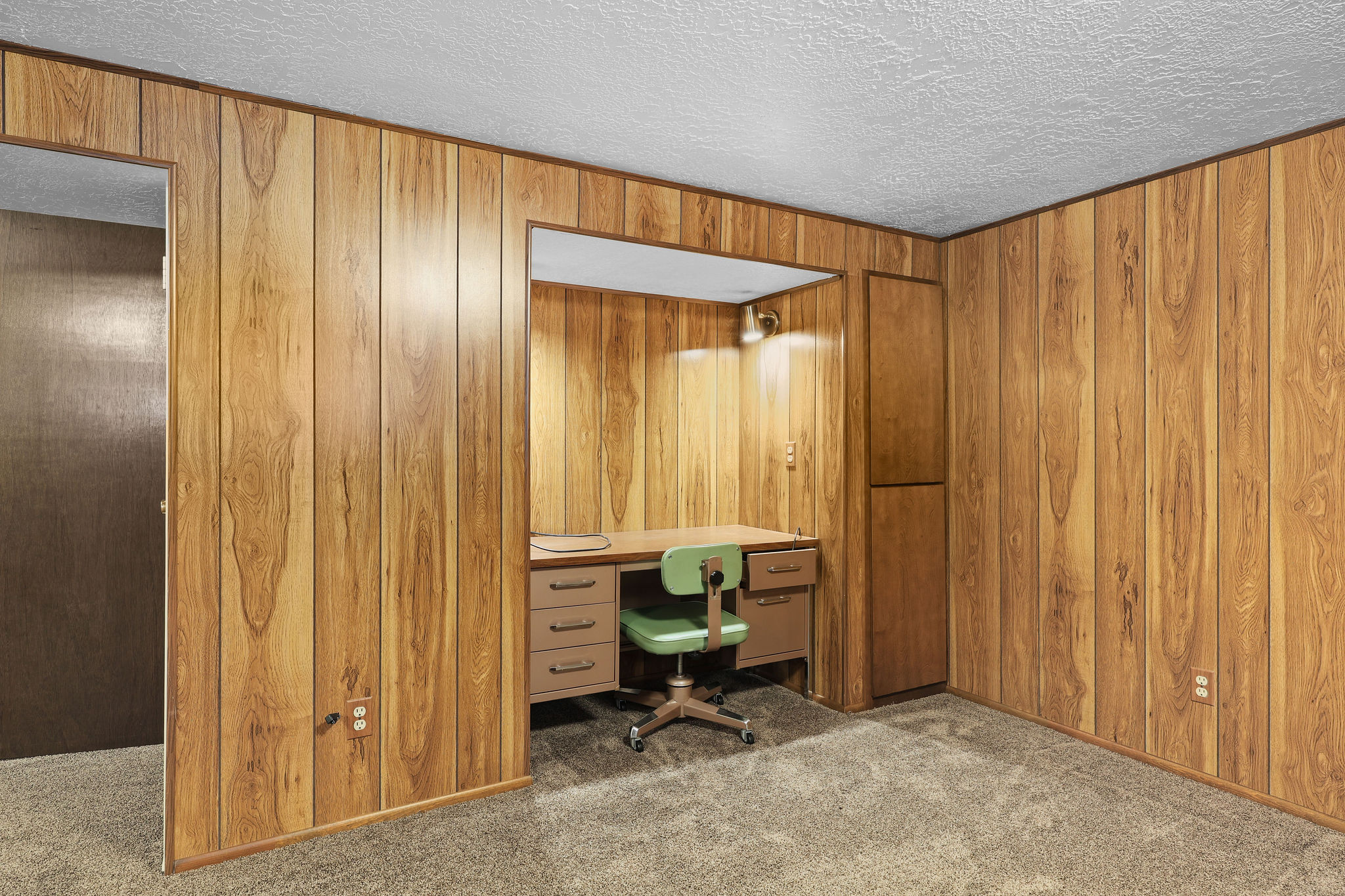 Office space with carpet flooring, a textured ceiling, and wood walls.