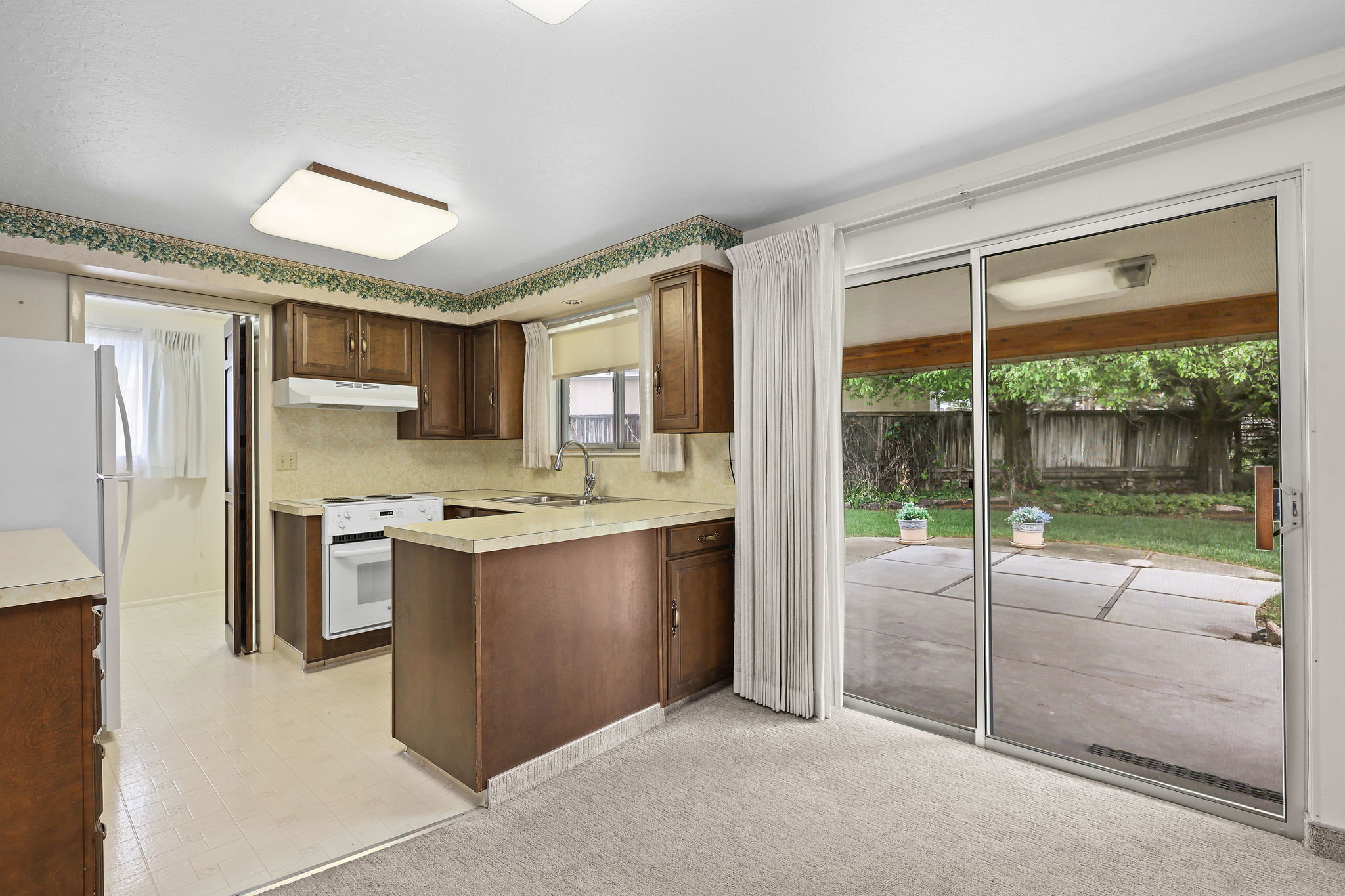 Kitchen with a peninsula, light countertops, white appliances, and light flooring. Sliding glass door access to patio.
