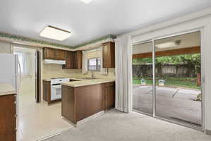 Kitchen with a peninsula, light countertops, white appliances, and light flooring. Sliding glass door access to patio.