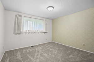 Unfurnished room featuring a textured ceiling, wallpapered walls, and carpet floors