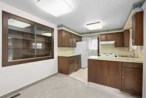 Kitchen featuring light countertops, a peninsula, freestanding refrigerator, and dark wood finish cabinetry