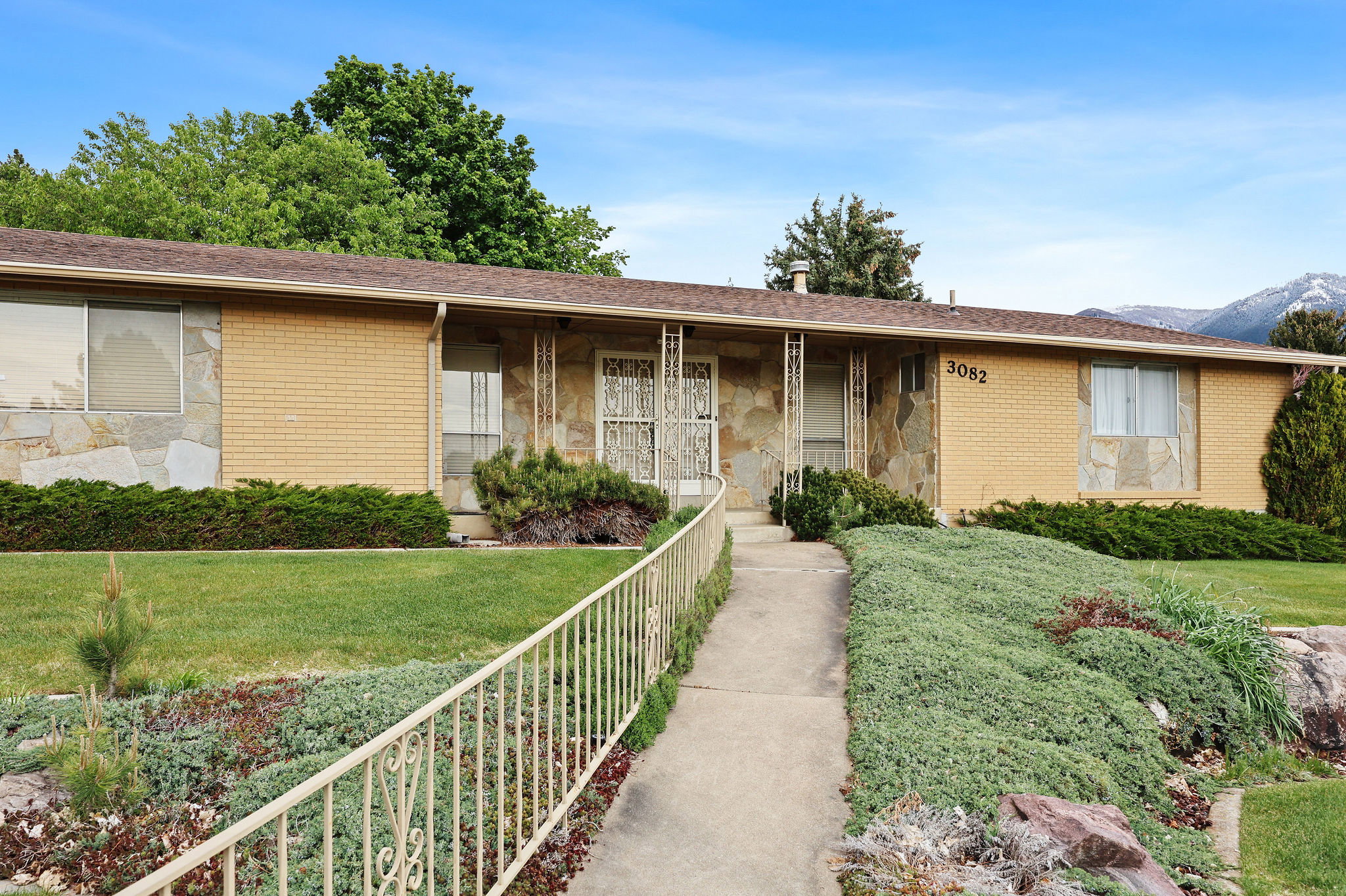 Ranch-style house featuring brick and stone, a front lawn, covered porch, a shingled roof.